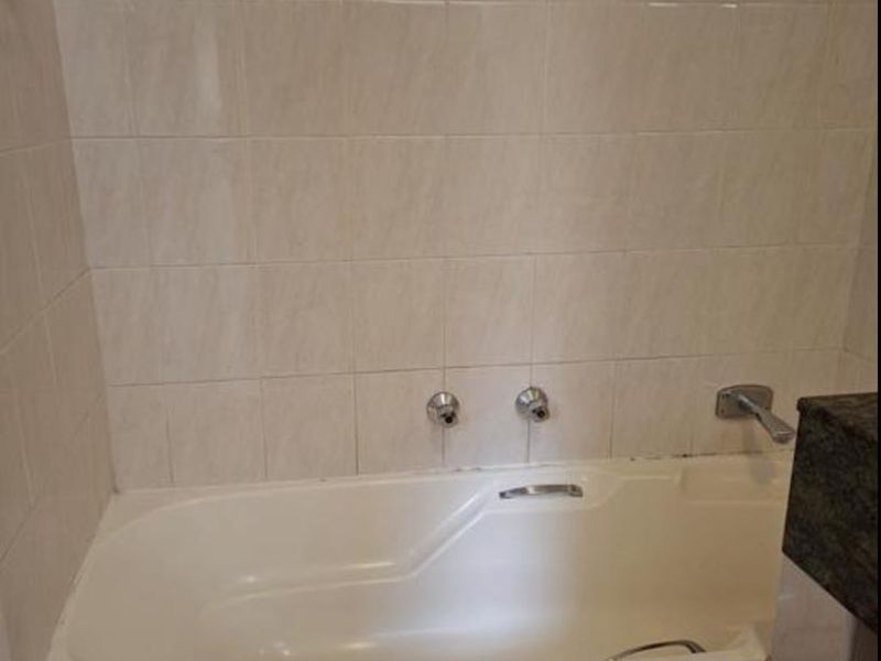 A functional bathroom featuring a built-in bathtub with tiled surround and wall tiling, providing a clean and neutral foundation for potential updates.