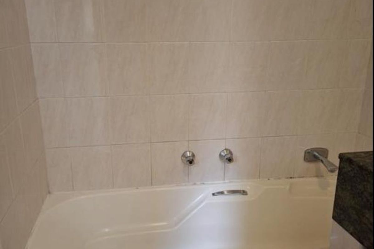 A functional bathroom featuring a built-in bathtub with tiled surround and wall tiling, providing a clean and neutral foundation for potential updates.