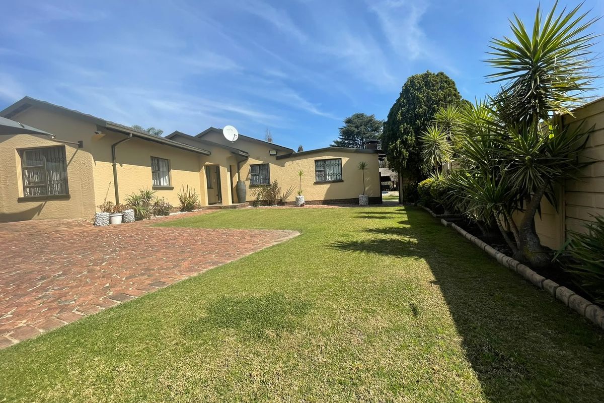 A well-maintained rear exterior view featuring a brick paved driveway, a neat lawn, and secure boundary walls.