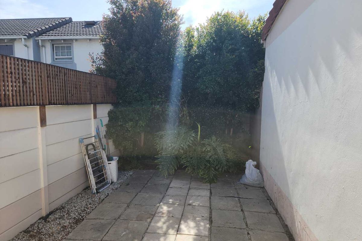 A private rear courtyard featuring a paved patio area, boundary walls with timber fencing, and established garden greenery.
