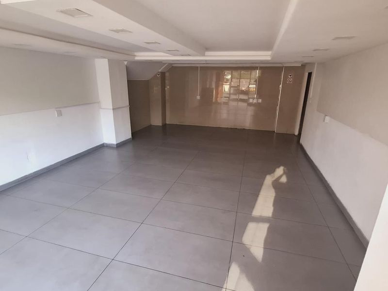 A spacious, empty open-plan area featuring modern large-format floor tiles, recessed ceiling lighting, and a glossy tiled feature wall.