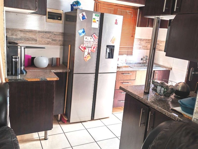 A functional kitchen featuring dark wood cabinetry, granite countertops, tiled backsplash, and ceramic floor tiles, providing a practical workspace.