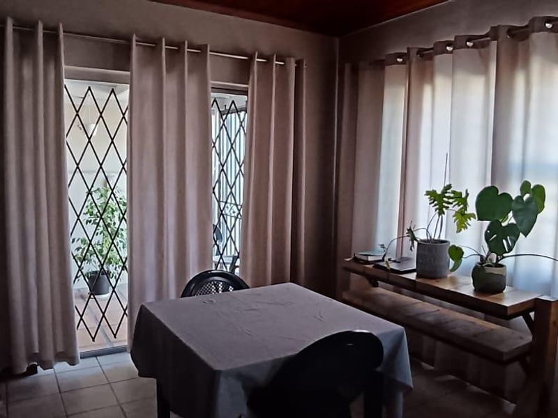A living area featuring tiled flooring, large windows with curtains, and a glass door leading to an outdoor space with security gates.