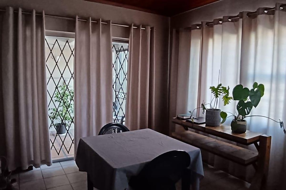 A living area featuring tiled flooring, large windows with curtains, and a glass door leading to an outdoor space with security gates.