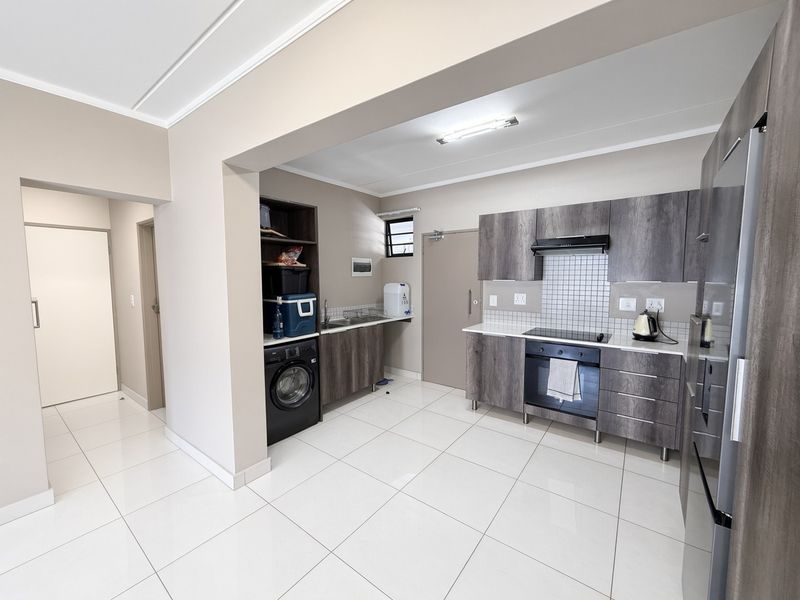 Modern kitchen featuring dark wood-grain cabinetry, integrated appliances, tiled flooring, and a functional layout with a dedicated laundry or scullery area.