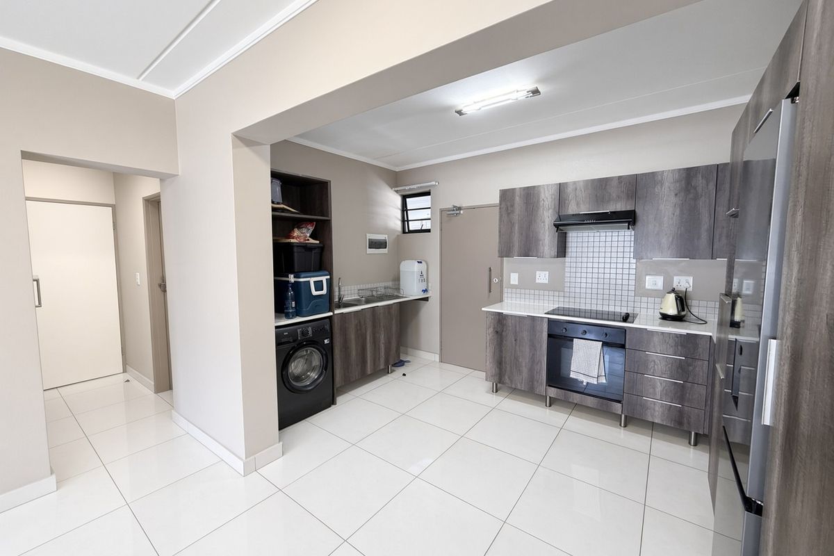 Modern kitchen featuring dark wood-grain cabinetry, integrated appliances, tiled flooring, and a functional layout with a dedicated laundry or scullery area.