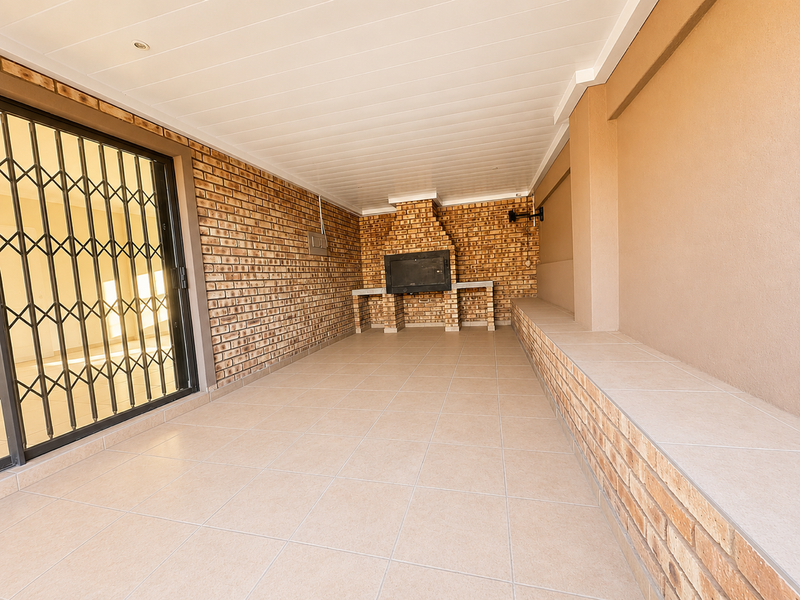 A spacious covered patio featuring a built-in brick braai, tiled flooring, and a built-in bench, providing an ideal area for outdoor entertaining.