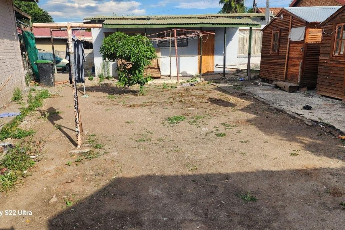 A rear exterior view of the property featuring a large unpaved yard area, a small timber outbuilding, and a covered patio section.