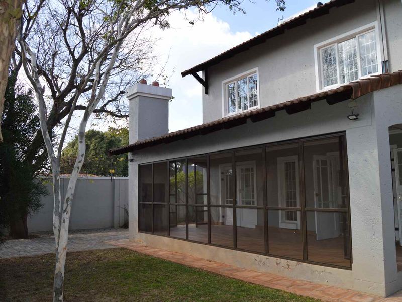 Rear view of the house featuring an enclosed patio area, tiled roof, and a chimney, set against a paved garden space.