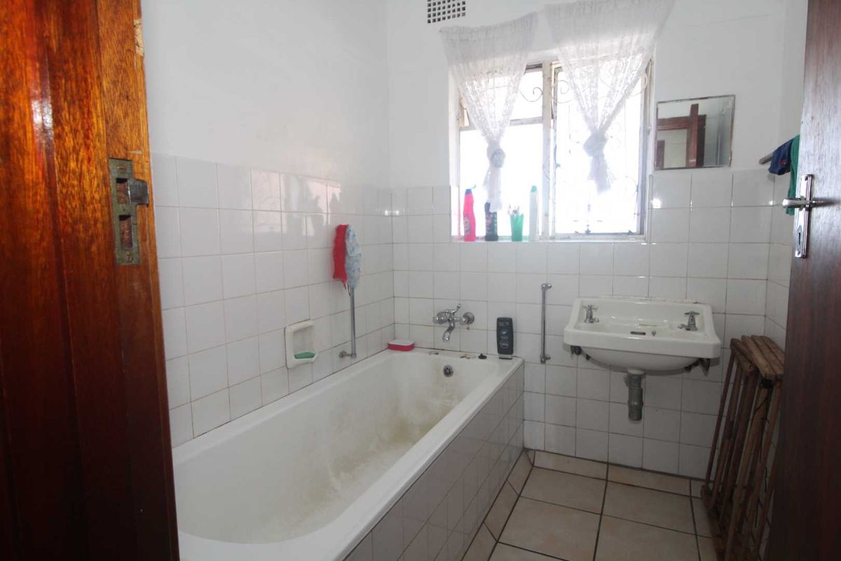 A dated bathroom featuring a standard bathtub, wall-mounted basin, and tiled walls, requiring cosmetic updates to modernize the space.