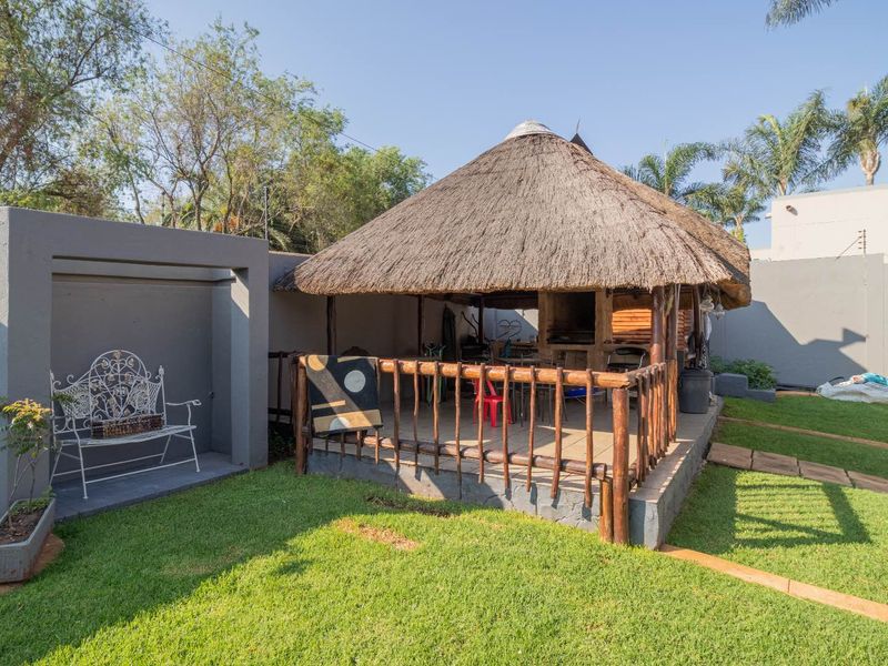 Outdoor thatched lapa area featuring a built-in braai, wooden railing, and paved flooring, set within a private garden space.