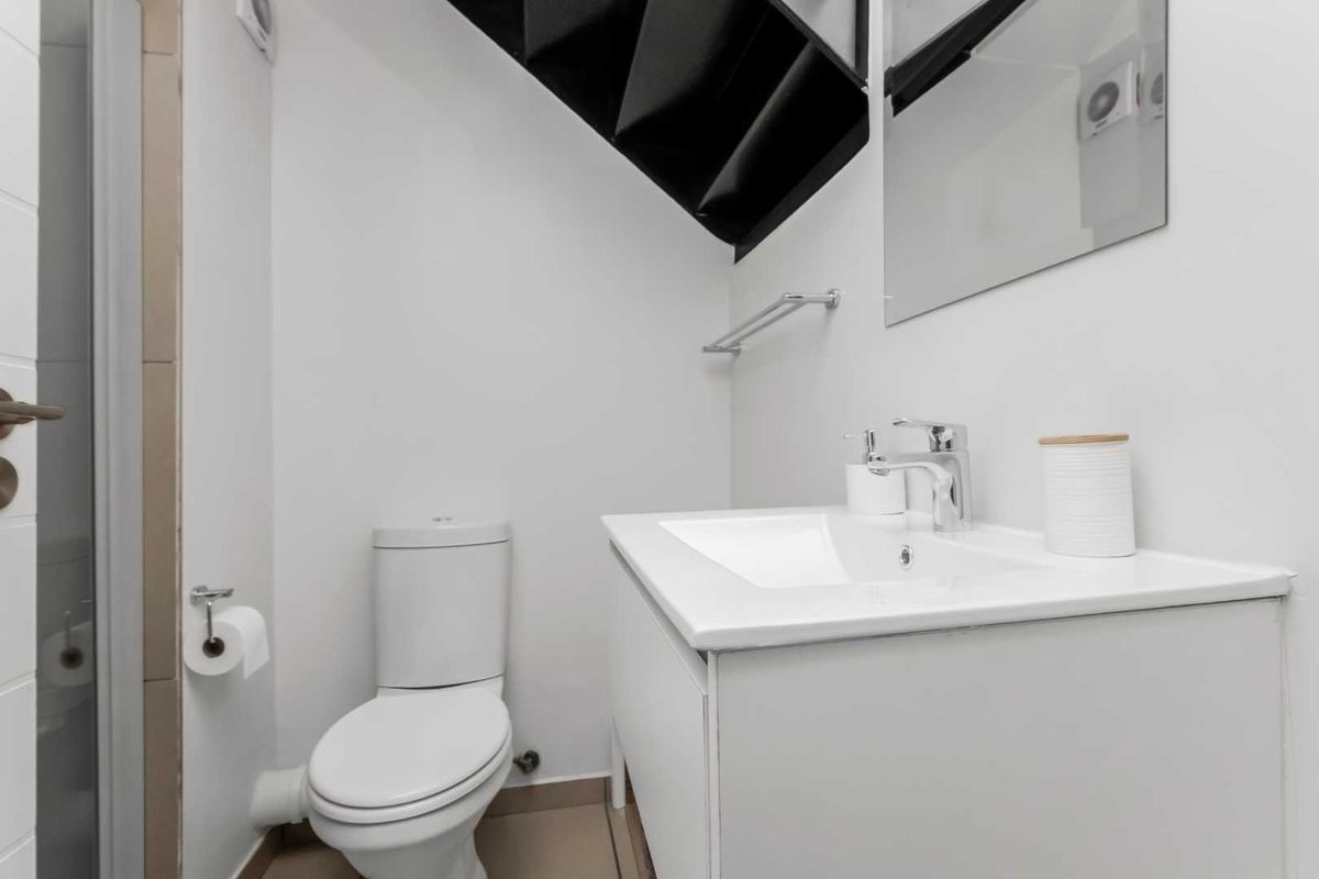 A compact bathroom featuring a modern vanity with integrated basin, a wall-mounted mirror, and a standard toilet, situated under a staircase.