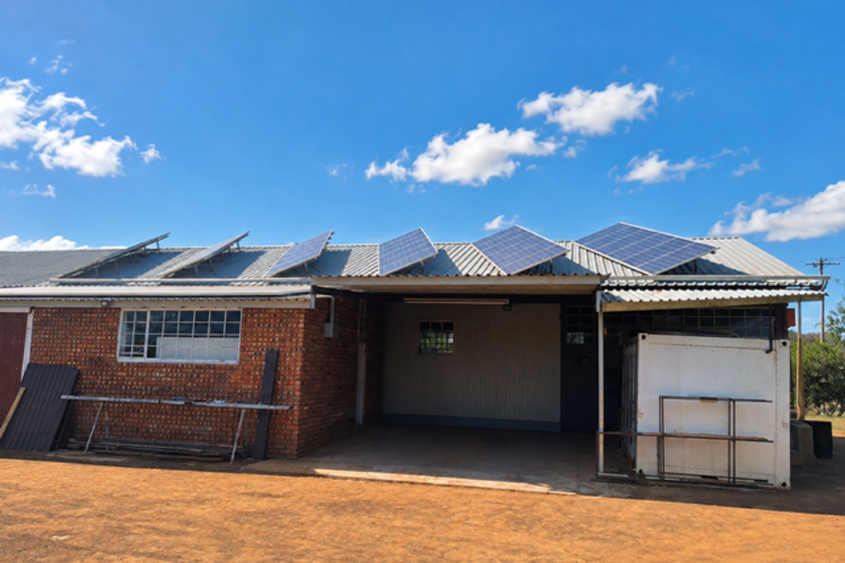 Rear view of a farm building featuring a corrugated metal roof with installed solar panels, brick exterior, and a covered carport area.