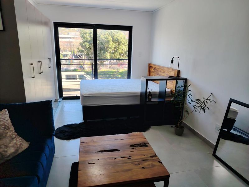 A modern bedroom featuring built-in cupboards, tiled flooring, and a large sliding glass door providing natural light and access to the exterior.