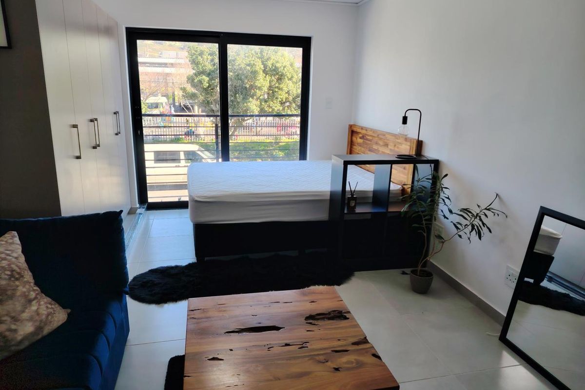 A modern bedroom featuring built-in cupboards, tiled flooring, and a large sliding glass door providing natural light and access to the exterior.