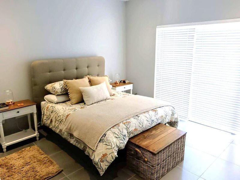 A bright bedroom featuring tiled flooring and a large sliding glass door with venetian blinds, providing ample natural light.