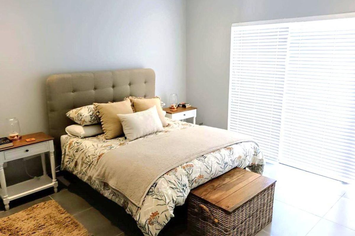 A bright bedroom featuring tiled flooring and a large sliding glass door with venetian blinds, providing ample natural light.