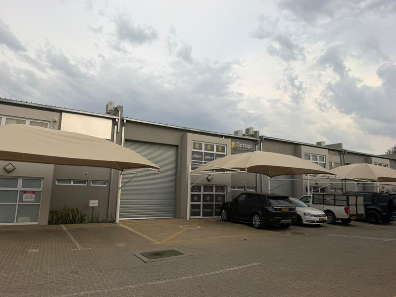 Front elevation of a commercial office and warehouse complex featuring roller shutter doors, paved parking bays, and shade cloth carports.