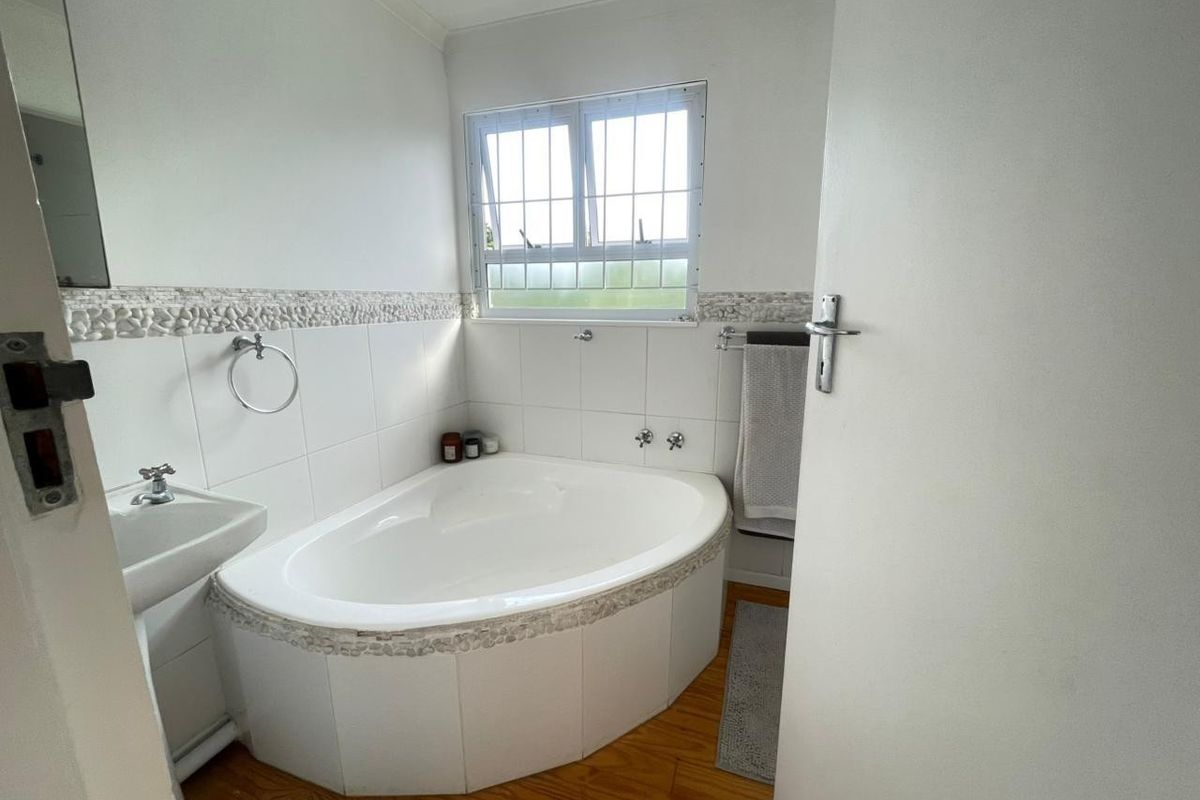 A functional bathroom featuring a corner bathtub, pedestal basin, and tiled wall accents with a window providing natural light.