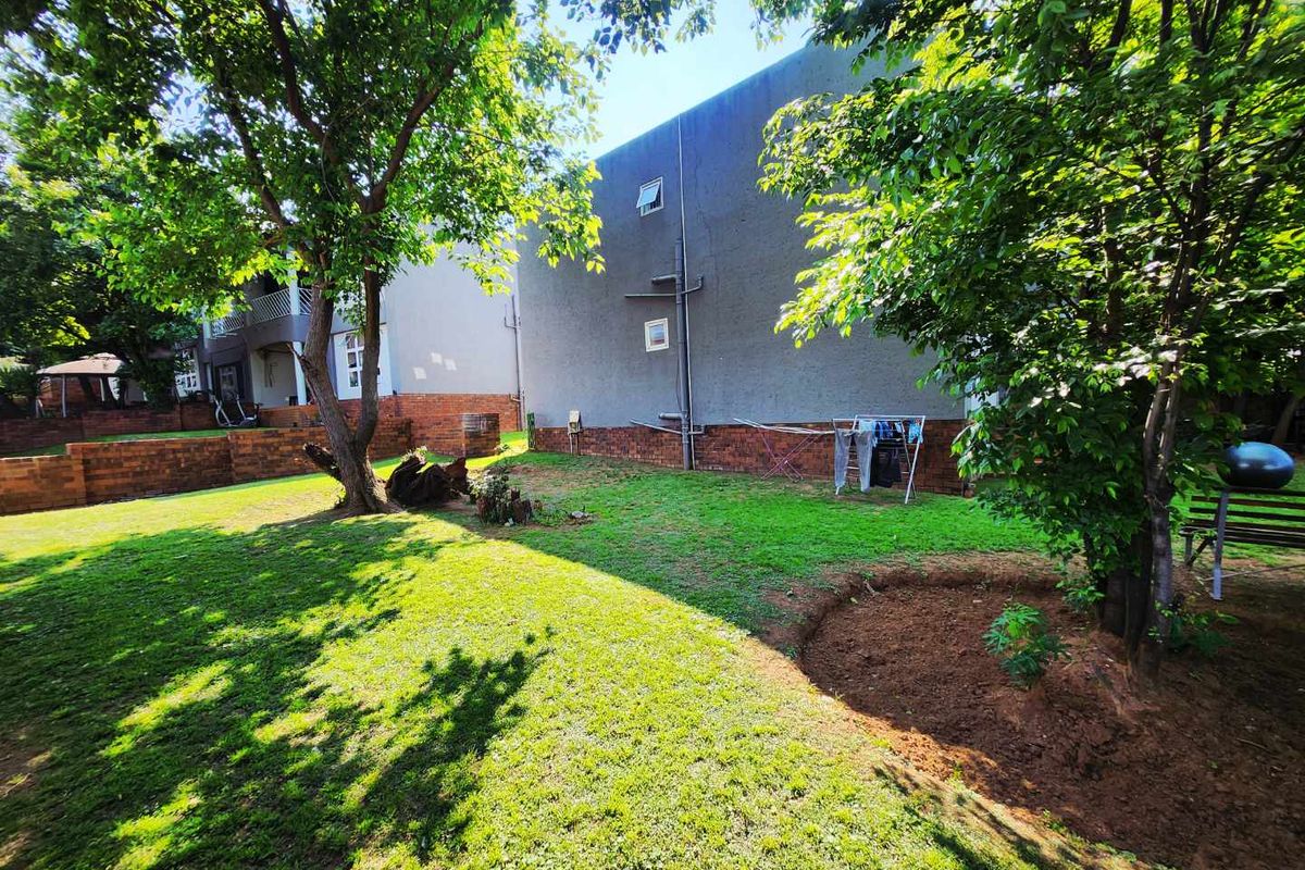 A spacious rear garden area featuring a lawn, mature trees, and a brick retaining wall adjacent to the townhouse exterior.
