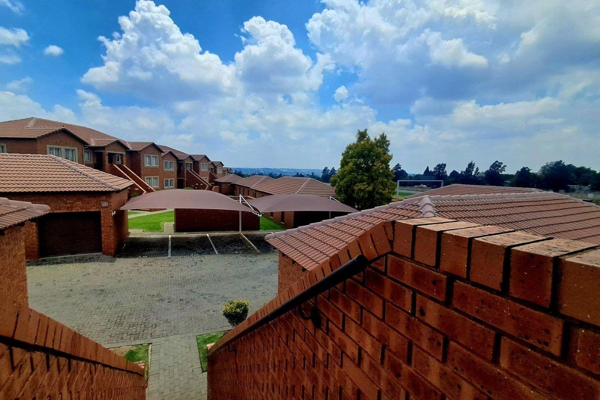 Elevated view of a townhouse complex featuring brick facades, tiled roofs, paved driveways, and covered parking bays.