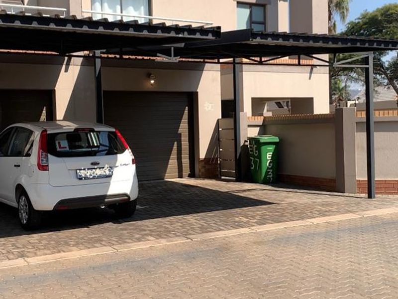 Front elevation of a townhouse featuring a paved driveway, a covered metal carport, and a secure garage entrance.