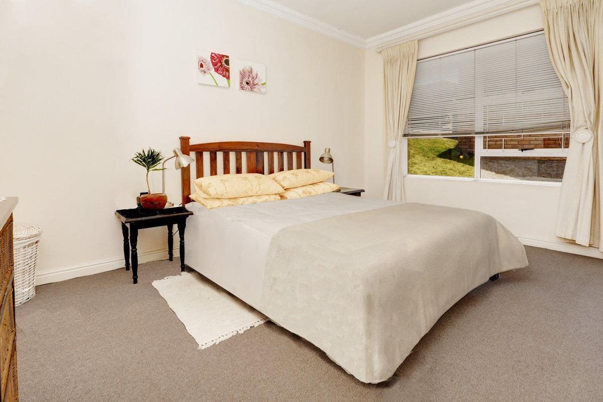 A carpeted bedroom featuring neutral walls, crown molding, and a window with fitted blinds and curtains.