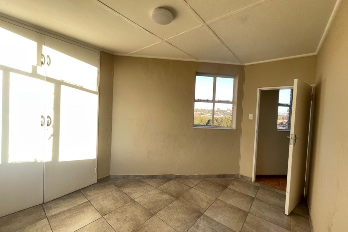 An empty bedroom featuring tiled flooring, built-in cupboards, and a view through the window.