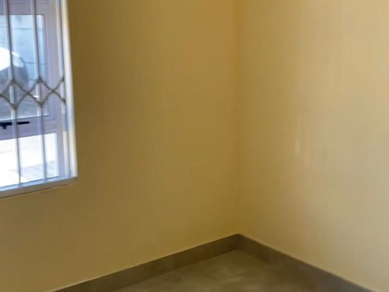 A clean, empty bedroom featuring neutral yellow walls, modern grey floor tiles, and a window fitted with a security gate.
