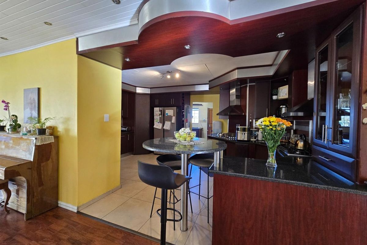 A kitchen featuring dark wood cabinetry, granite countertops, a breakfast bar, and recessed lighting, with a distinct architectural bulkhead ceiling feature.