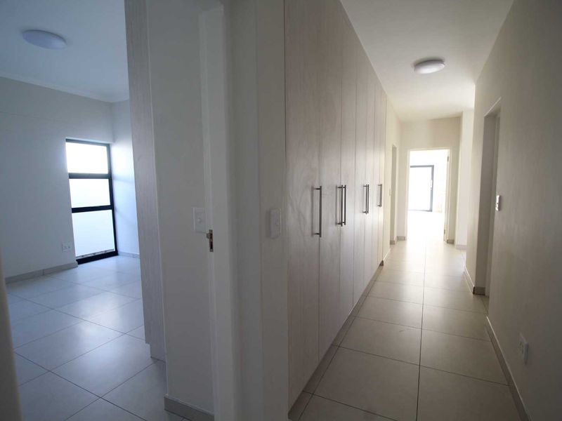 A bright, modern hallway featuring neutral tiled flooring and extensive built-in storage cupboards, leading towards an open living space.
