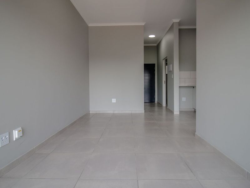 A bright, empty open-plan living area featuring neutral grey walls, large format floor tiles, and recessed lighting, offering a clean canvas for interior design.