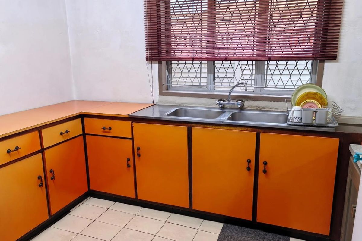 A dated kitchen featuring orange cabinetry, laminate countertops, a double bowl stainless steel sink, and ceramic floor tiles.