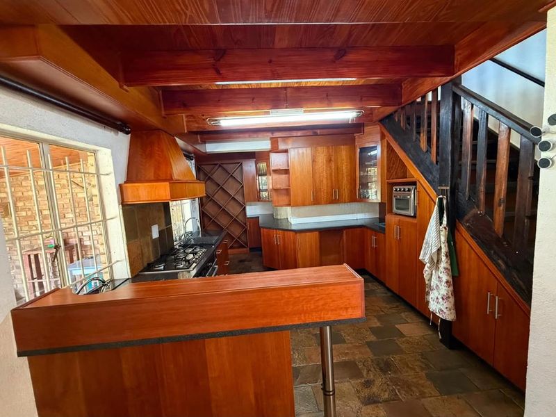 A rustic kitchen featuring extensive wooden cabinetry, built-in appliances, exposed timber ceiling beams, and slate tile flooring, with an integrated staircase.