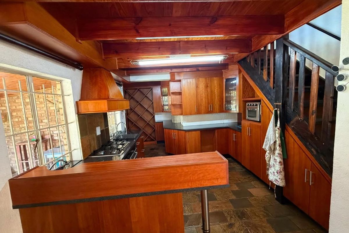 A rustic kitchen featuring extensive wooden cabinetry, built-in appliances, exposed timber ceiling beams, and slate tile flooring, with an integrated staircase.