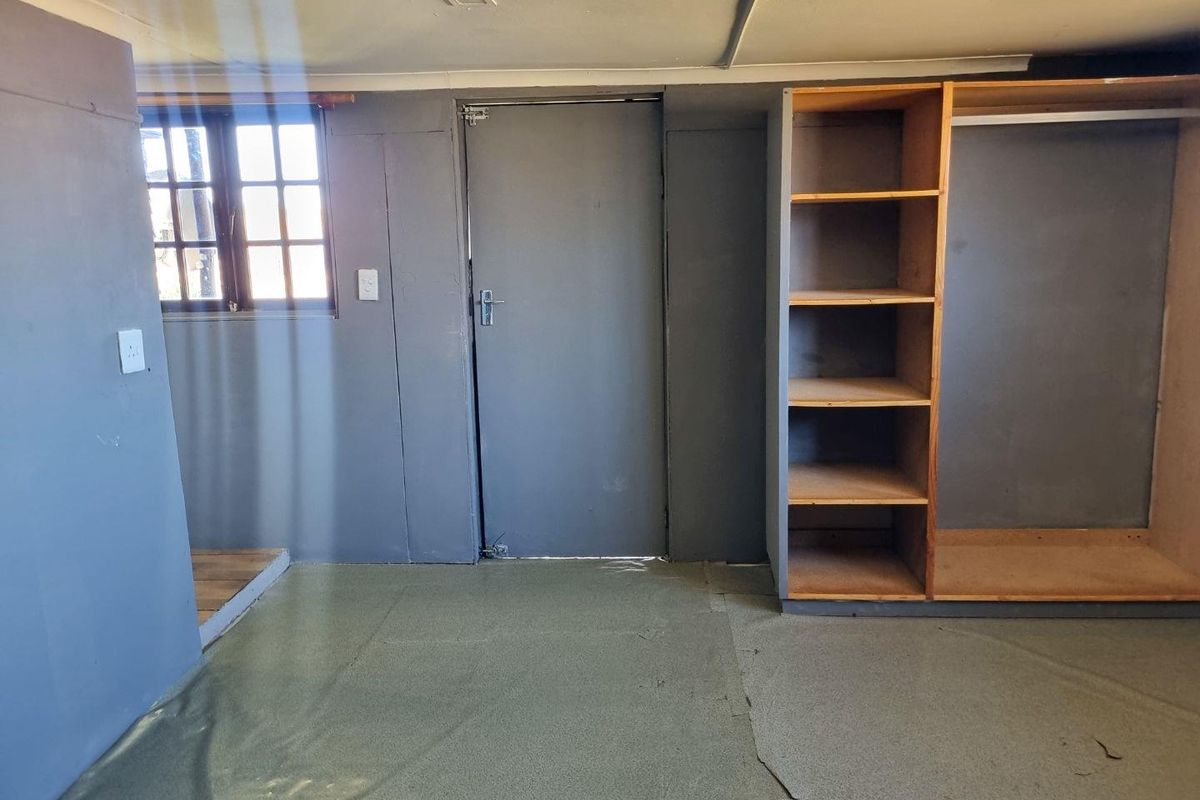 A bedroom featuring built-in shelving and storage, a window with grid detailing, and a single door entrance.