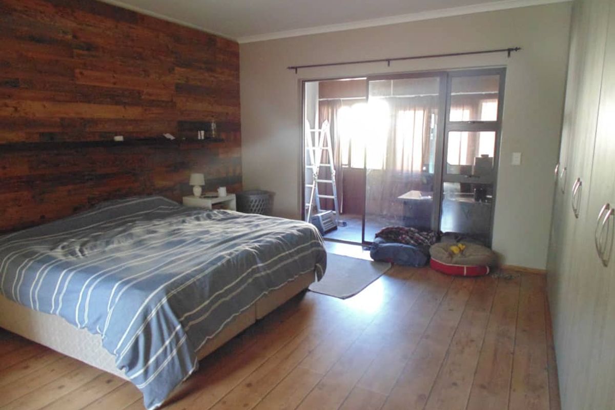Spacious bedroom featuring a rustic timber feature wall, built-in wardrobes, and sliding glass doors providing direct access to an outdoor patio area.