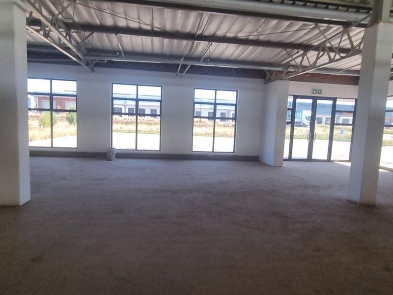 Spacious open-plan industrial unit featuring exposed steel roof trusses, concrete columns, and large windows providing ample natural light.