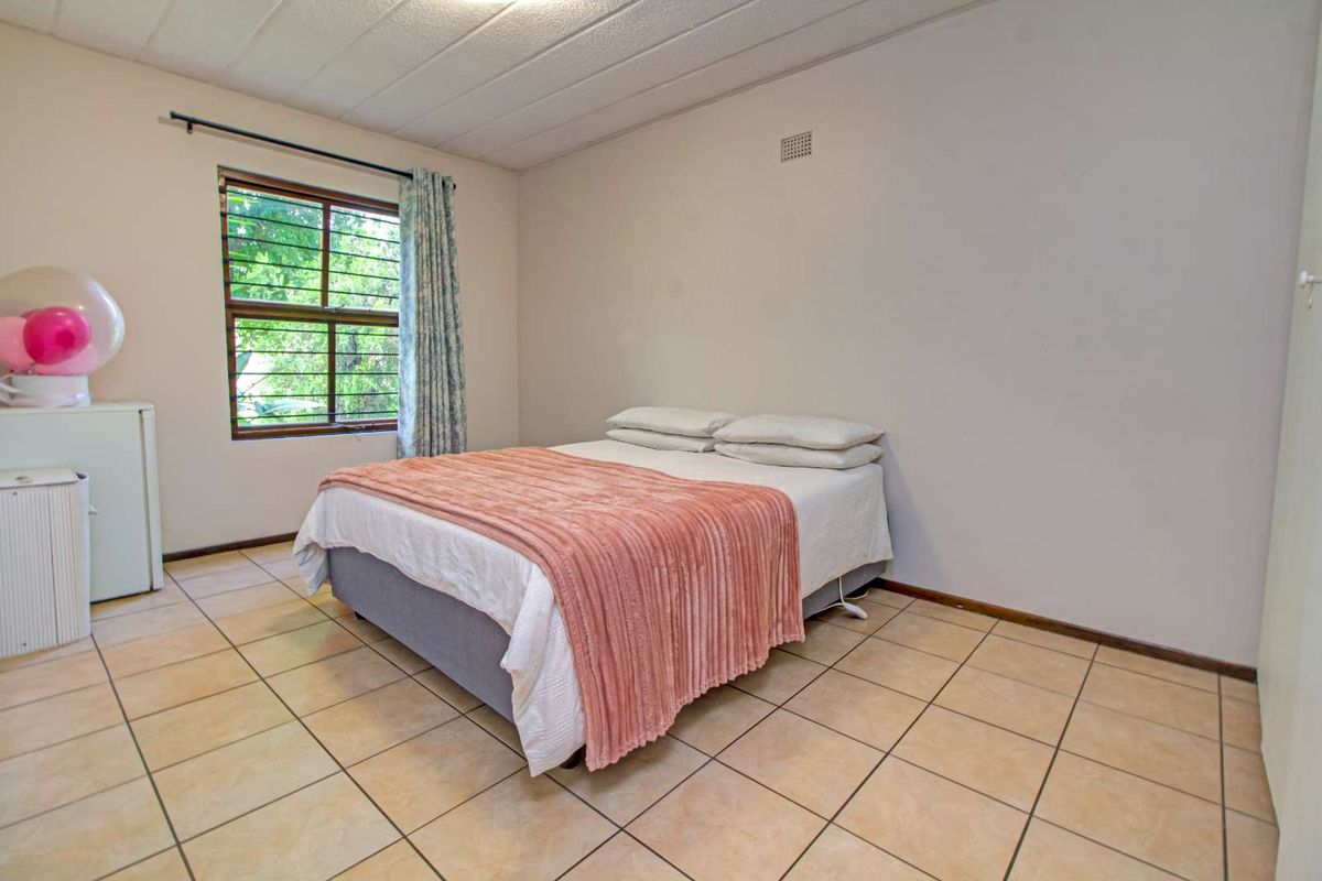A bedroom featuring tiled flooring, a window with security bars, and a textured ceiling finish.