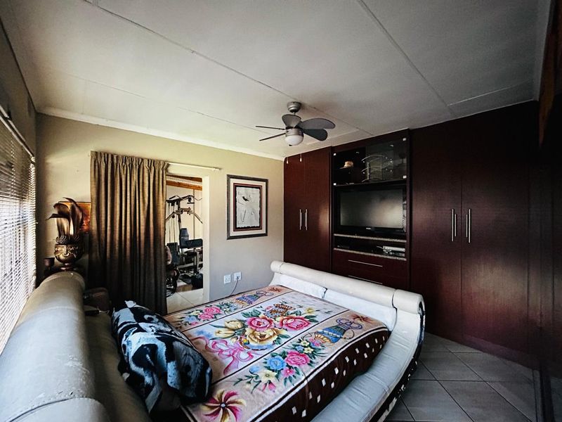 A bedroom featuring built-in dark wood cabinetry, a ceiling fan, and tiled flooring, with an adjacent room visible through the doorway.