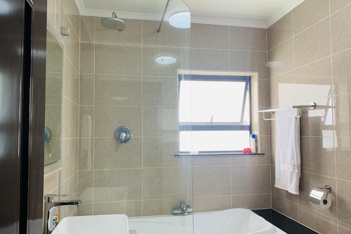 Modern bathroom featuring a built-in bathtub, glass shower screen, rainfall showerhead, and neutral wall tiling.