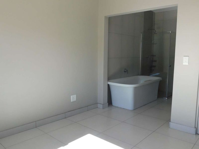 A modern, empty bathroom featuring a freestanding bathtub, a glass-enclosed shower, and neutral floor and wall tiling.