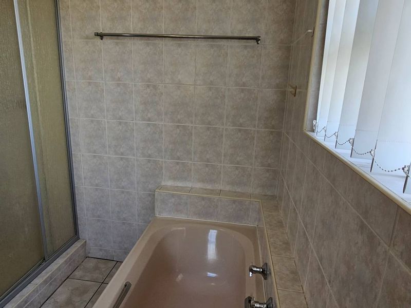 A functional bathroom featuring a built-in bathtub, a separate shower enclosure, and neutral wall tiling.