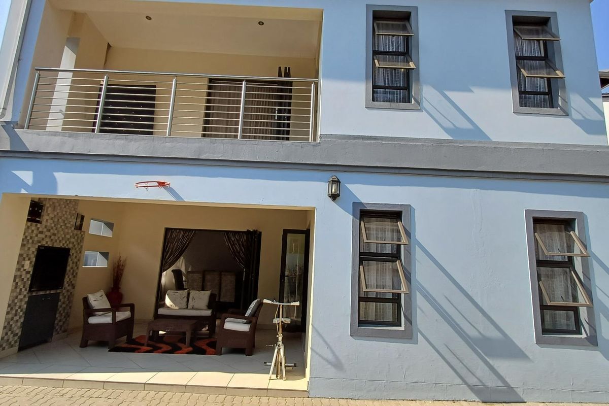 A two-story rear exterior view featuring a covered ground-floor patio, a first-floor balcony with stainless steel railings, and modern awning-style windows.