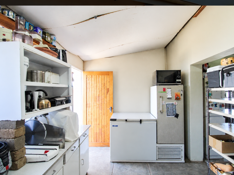 A functional scullery or utility area featuring built-in cabinetry, concrete flooring, and a timber door, requiring some ceiling maintenance.