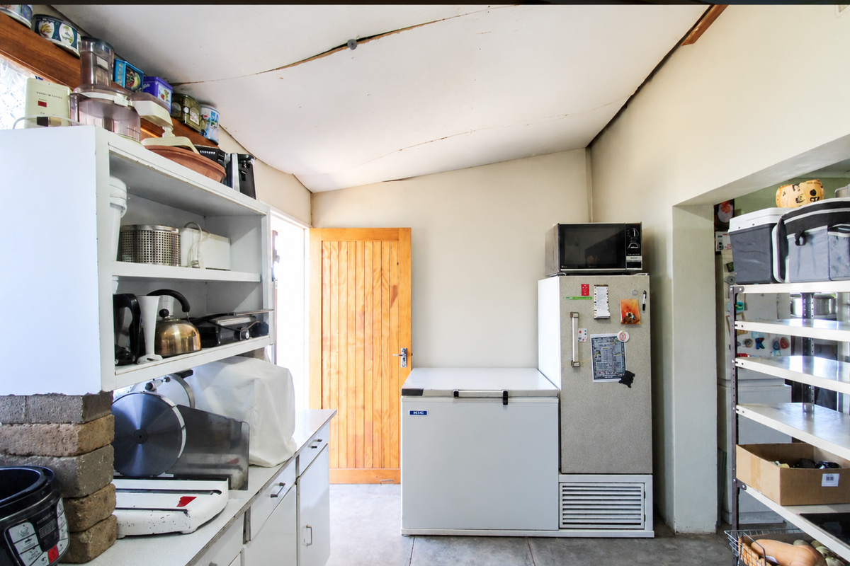 A functional scullery or utility area featuring built-in cabinetry, concrete flooring, and a timber door, requiring some ceiling maintenance.