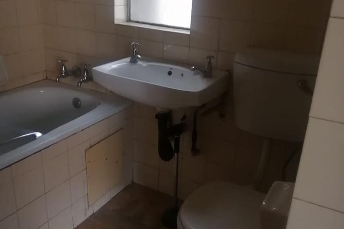 A dated bathroom featuring a bathtub, wall-mounted basin, and toilet with tiled walls, requiring renovation to update finishes and fixtures.