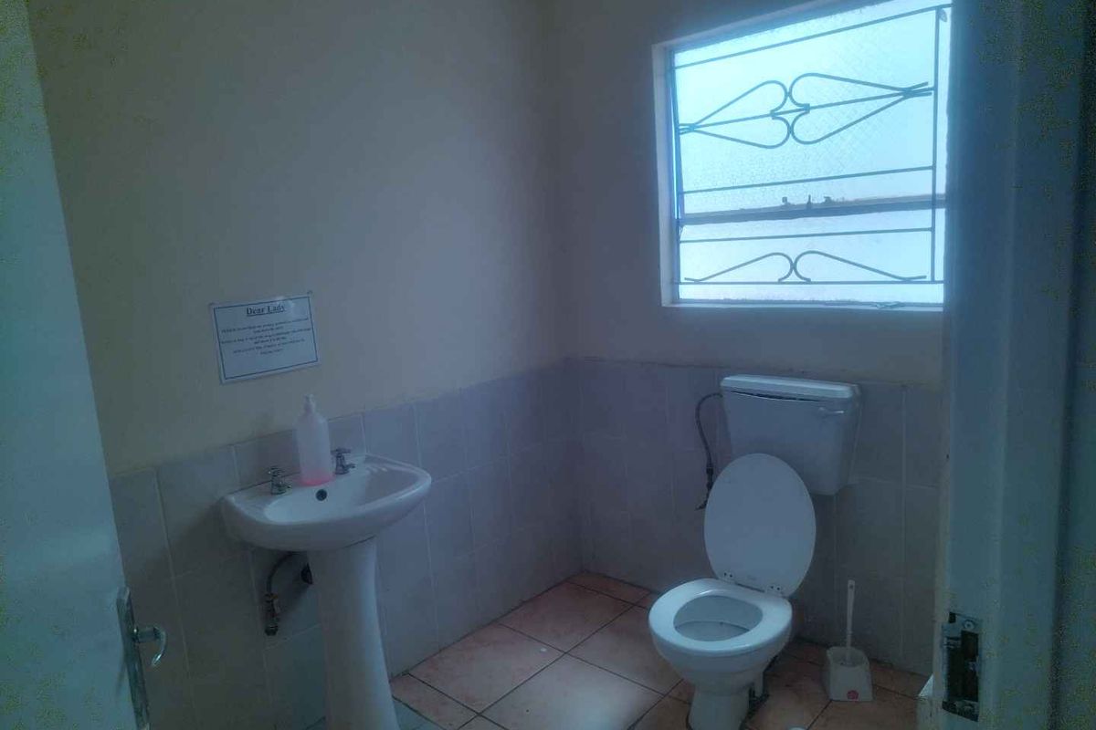 A functional office restroom featuring a pedestal basin, standard toilet, and a window with security bars.