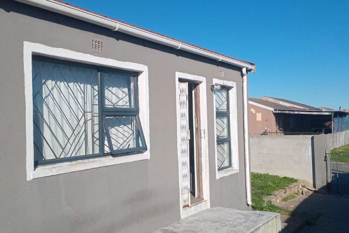 Front elevation of a residential house featuring grey exterior walls, aluminium window frames with security bars, and a concrete entrance porch.