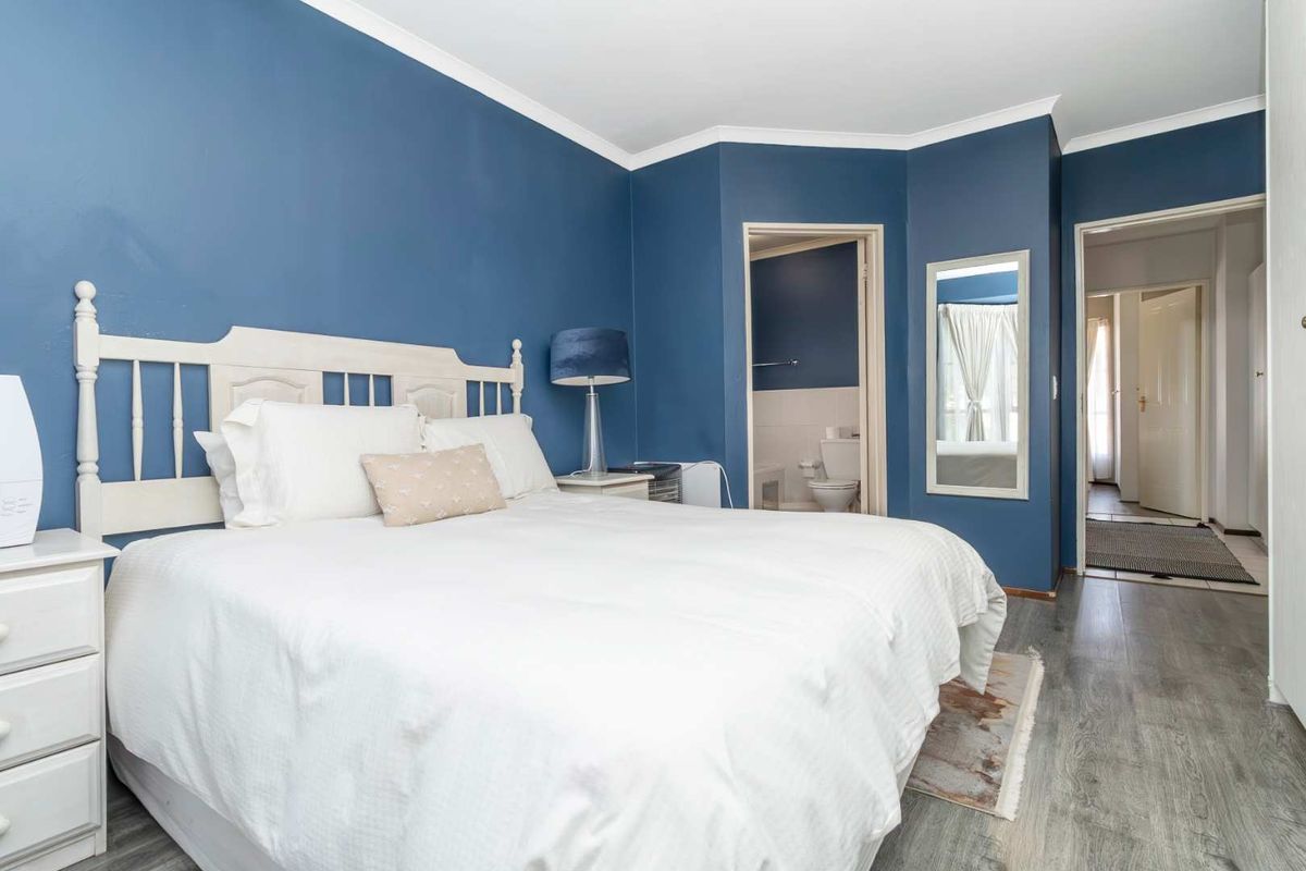 A bedroom featuring blue painted walls, wood-look laminate flooring, and an en-suite bathroom entrance.
